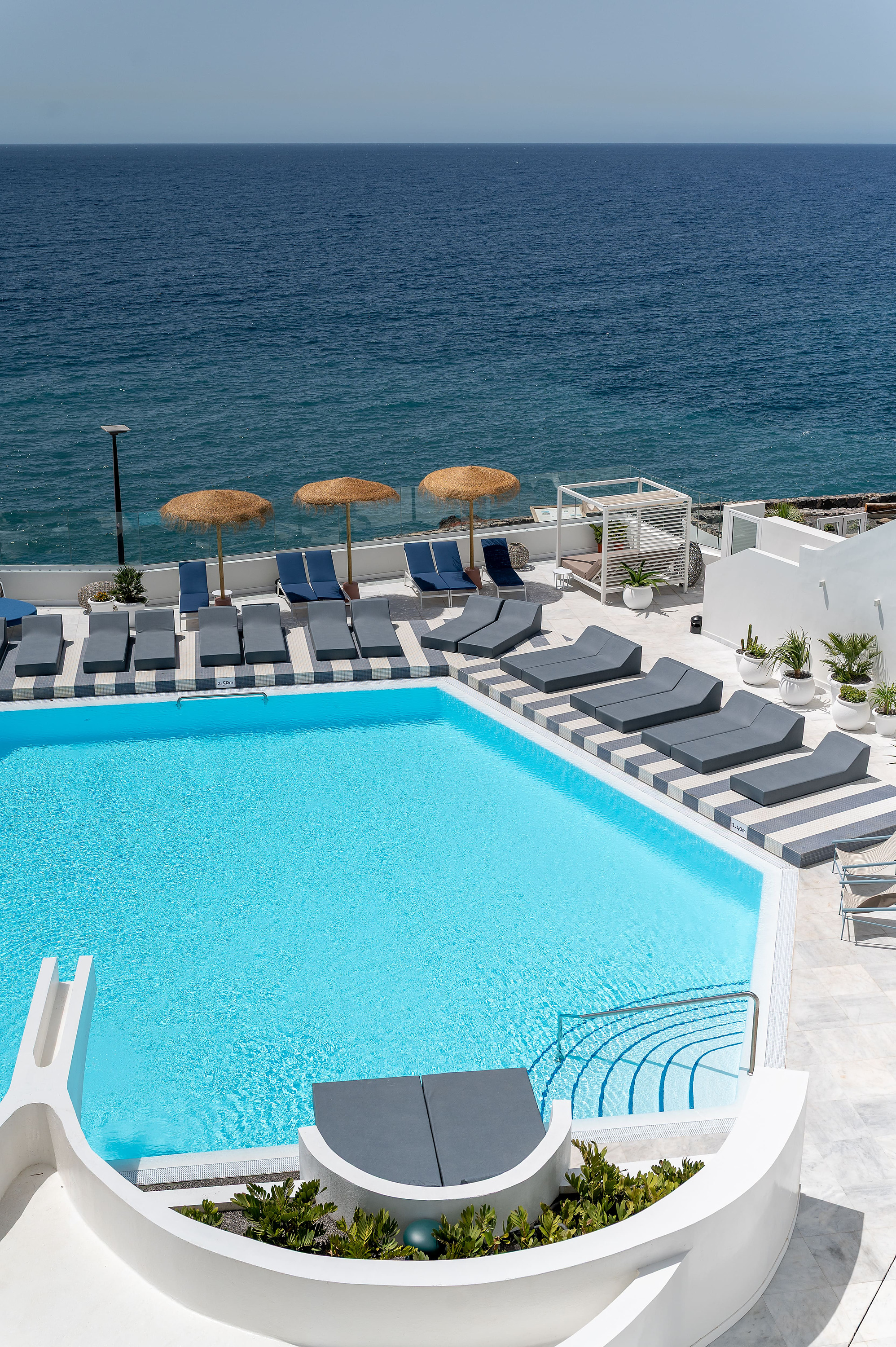 Piscina azul y tumbonas en The Salmar con vista al mar.