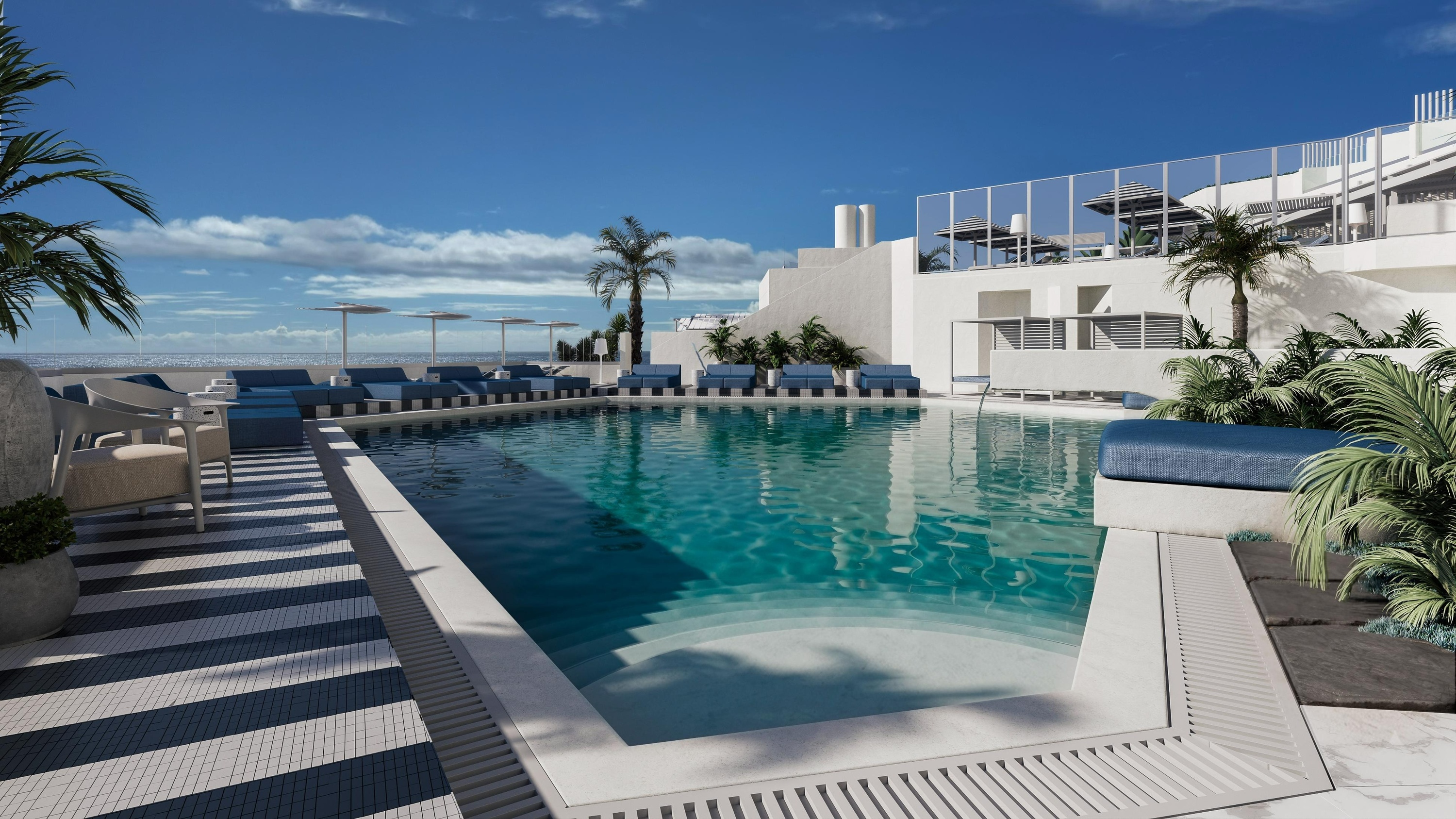 A modern outdoor swimming pool area with blue lounge seating, white architecture, palm trees, and a distant ocean view under a partly cloudy sky.