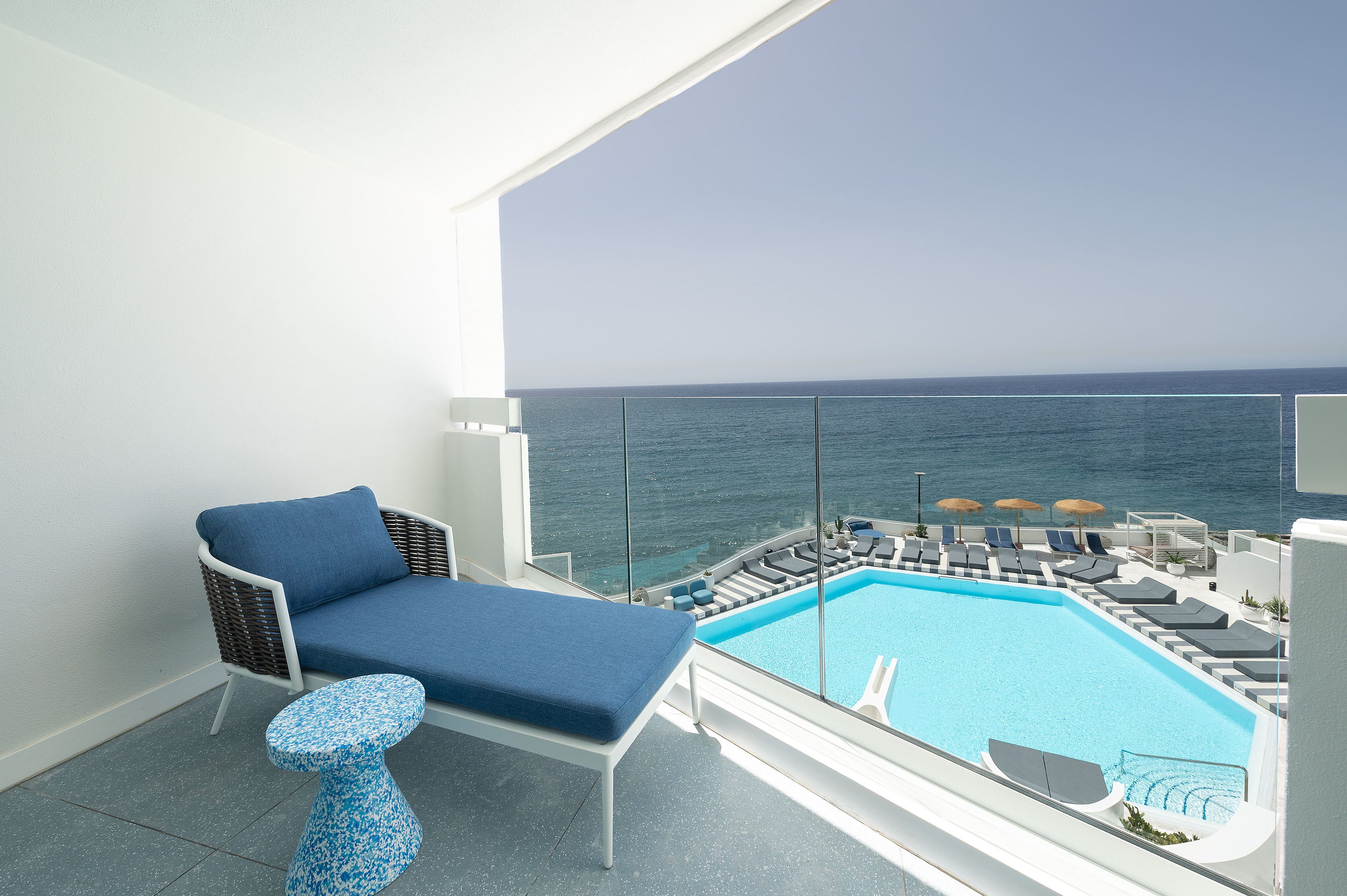 Balcón privado con tumbona azul y vista a la piscina infinita Satocan: The Salmar y el mar.