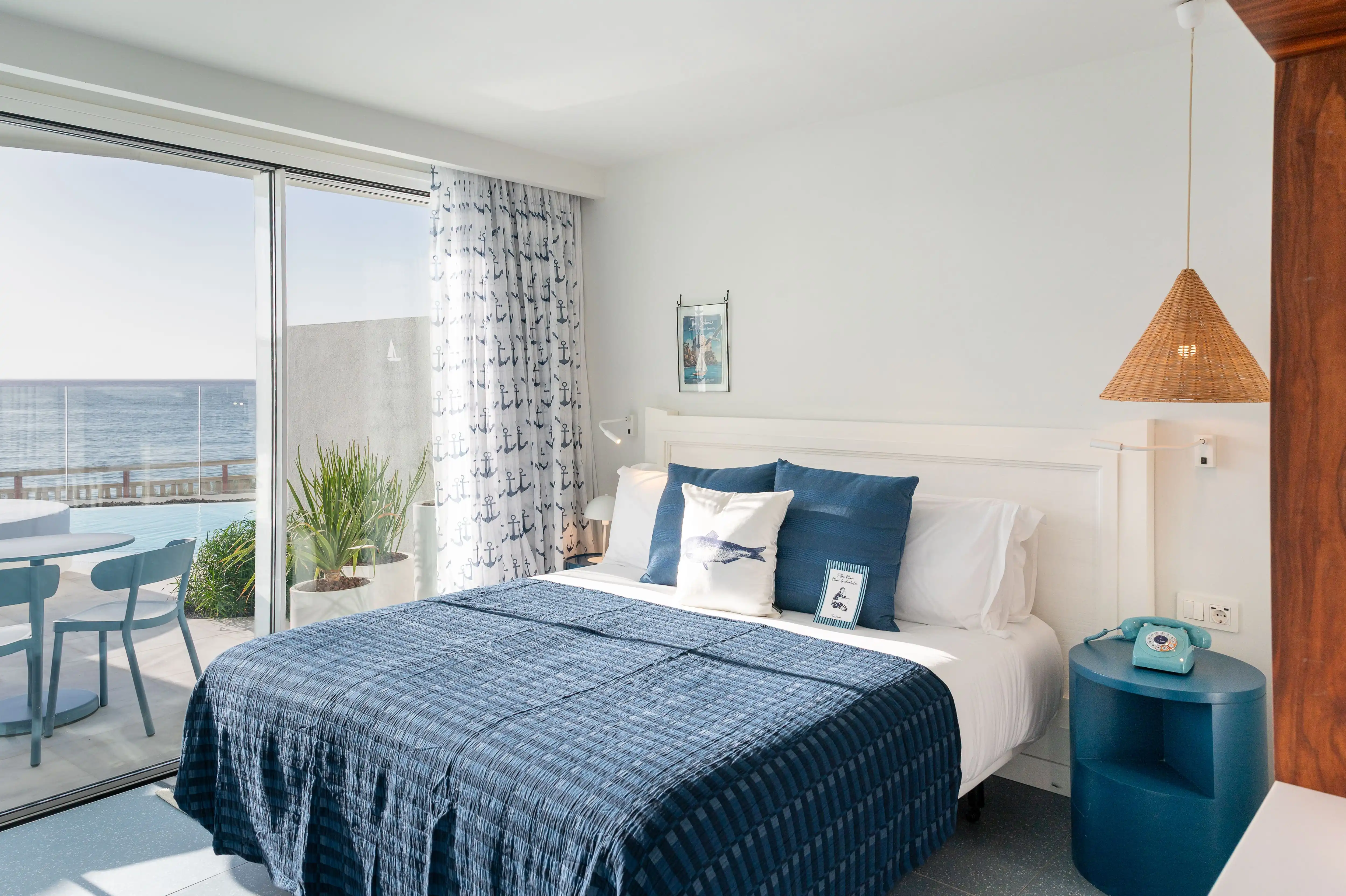 Habitación de hotel con cama azul, ventana al mar y balcón privado. The Salmar
