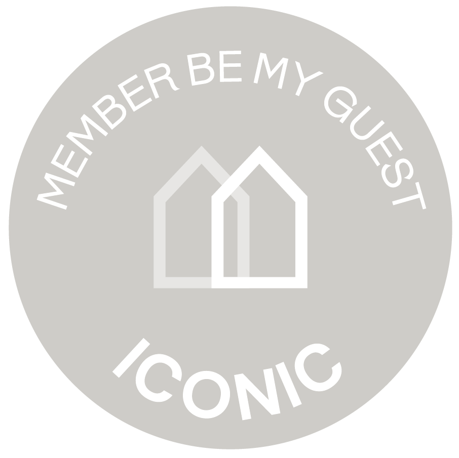 Un círculo gris claro con los textos "MEMBER BE MY GUEST" y "ICONIC" junto a dos siluetas de casas, todo sobre un fondo negro.