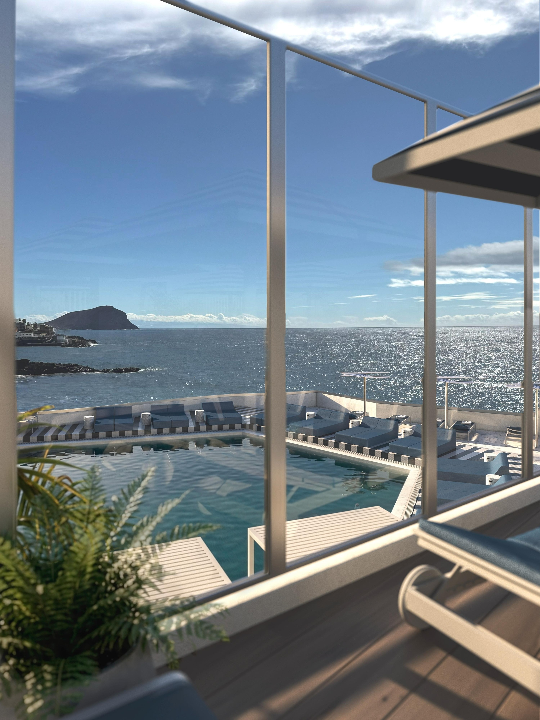 A modern balcony overlooks a resort pool and the sparkling ocean, with a distant island under a bright blue sky.