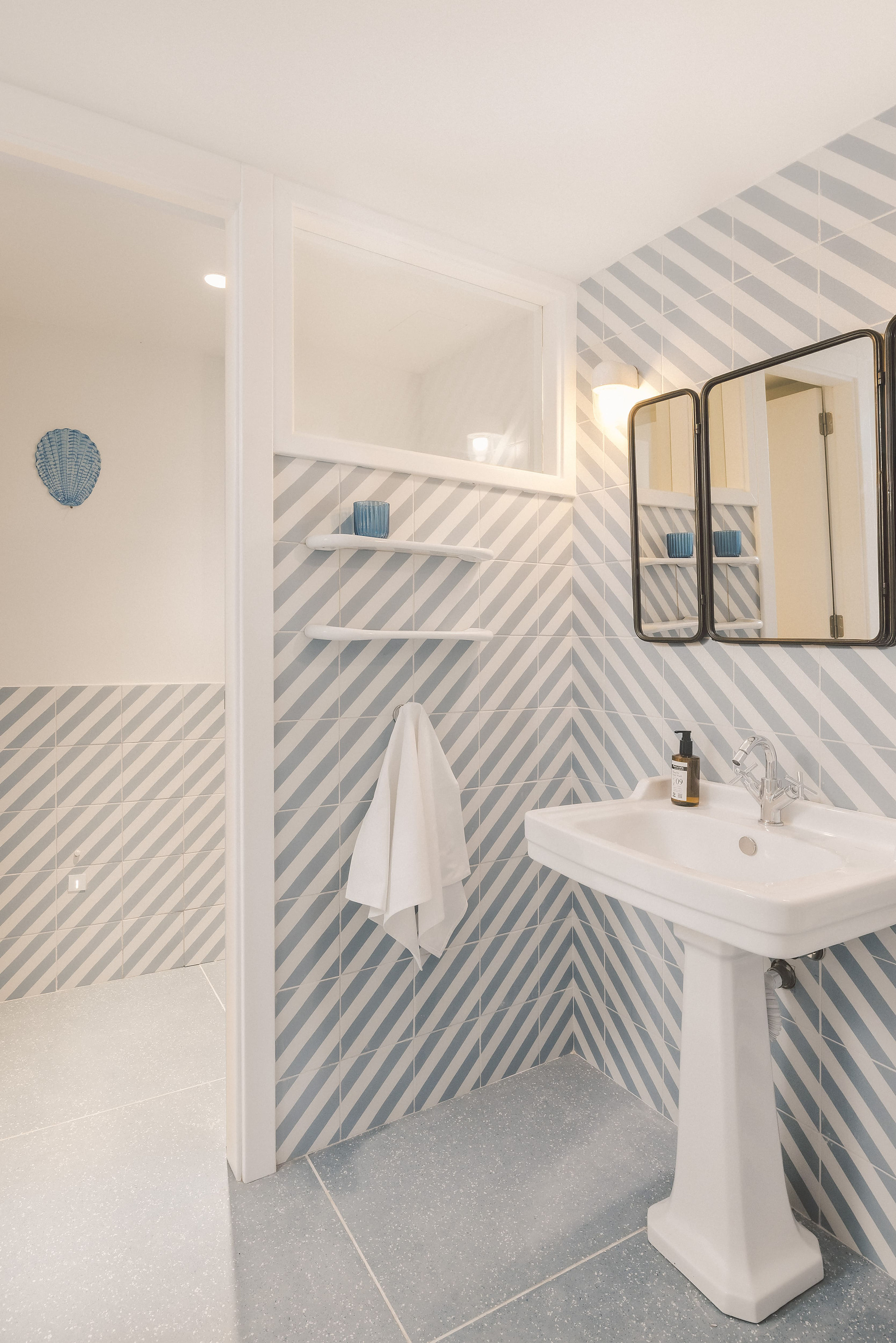 Baño moderno con azulejos diagonales azul claro y blanco, lavabo sobre pedestal y espejo triple. Satocan: The Salmar