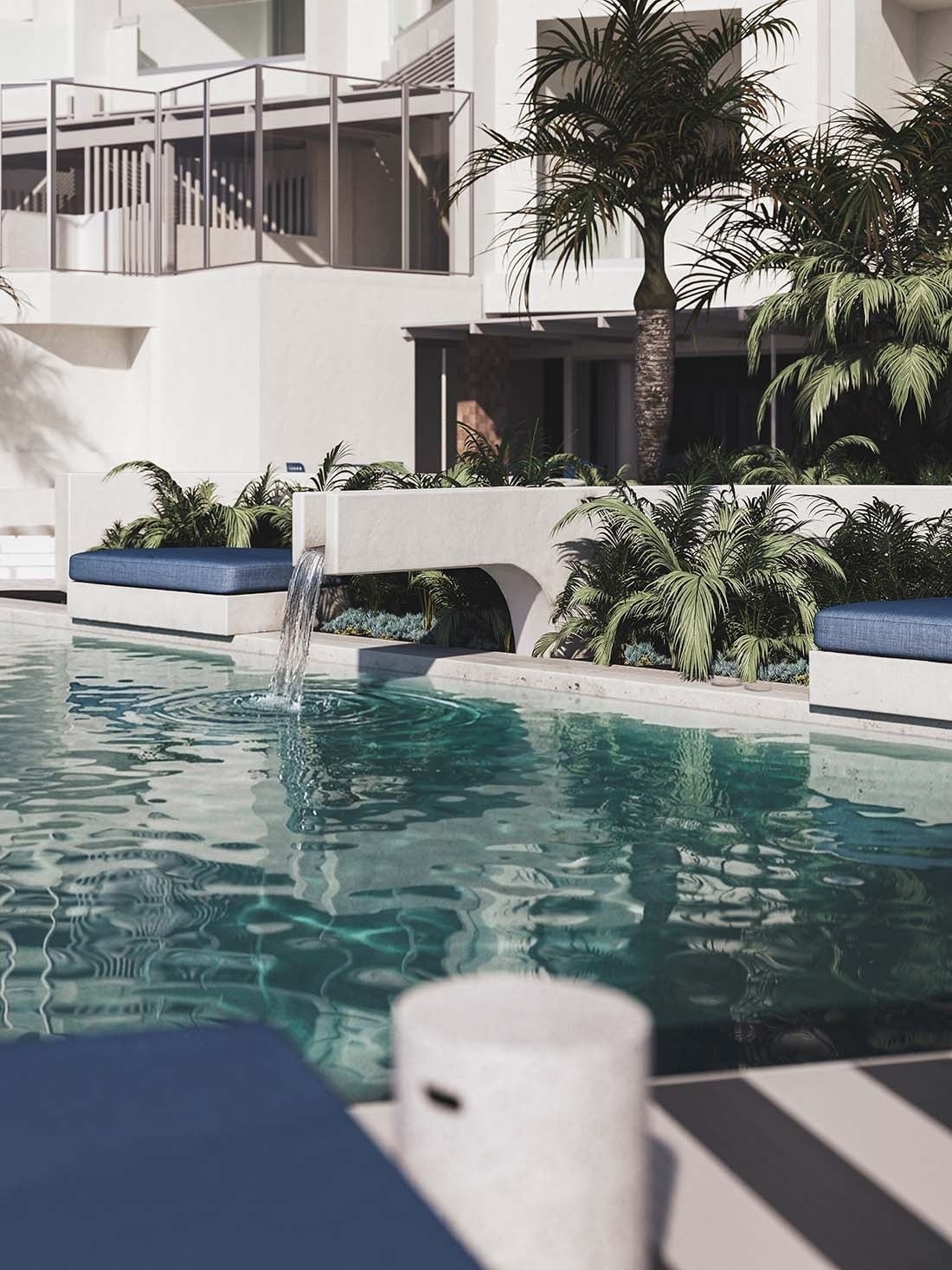 Piscina de diseño del hotel The Salmar con cascada de agua moderna, vegetación tropical y camas balinesas con textiles azules bajo el sol de Tenerife.
