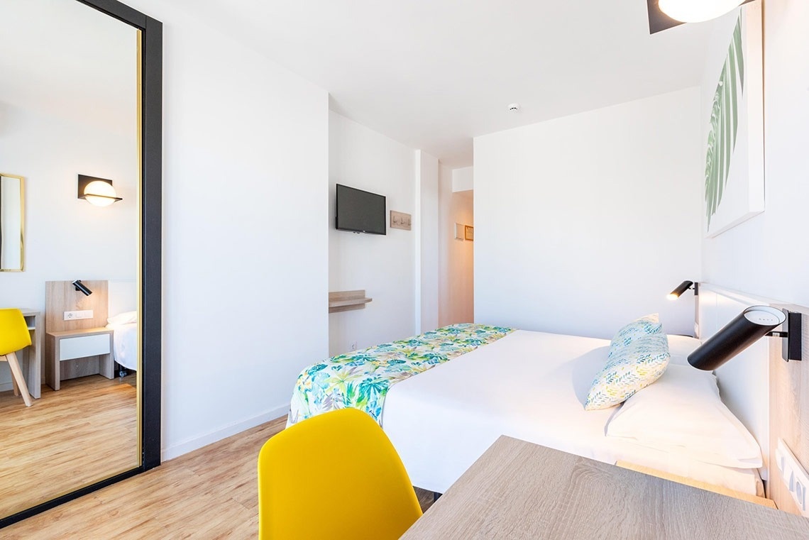 Habitación de hotel moderna y luminosa con cama doble, decoración vibrante y espejo de cuerpo entero.