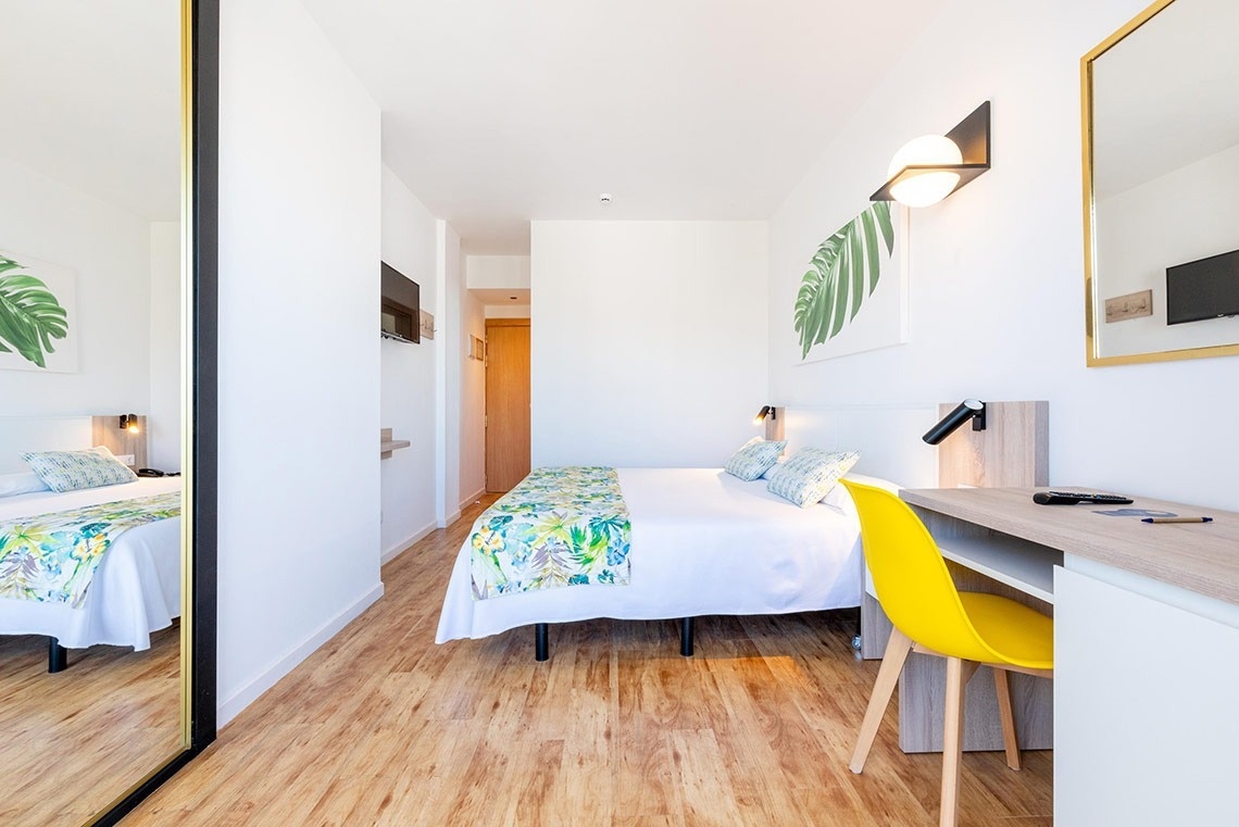 Habitación de hotel luminosa y moderna con cama, escritorio y decoración tropical.