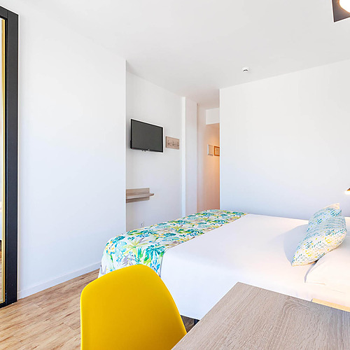 Habitación moderna con cama cómoda, espejo grande y silla amarilla, ideal para tu Dorobe: Hotel San Fermin.