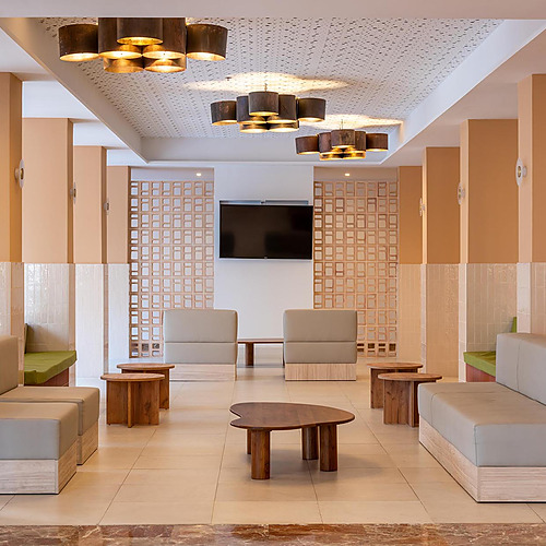 Sala de espera de hotel con sofás grises, mesas de madera y lámparas modernas. Dorobe: Hotel San Fermin.