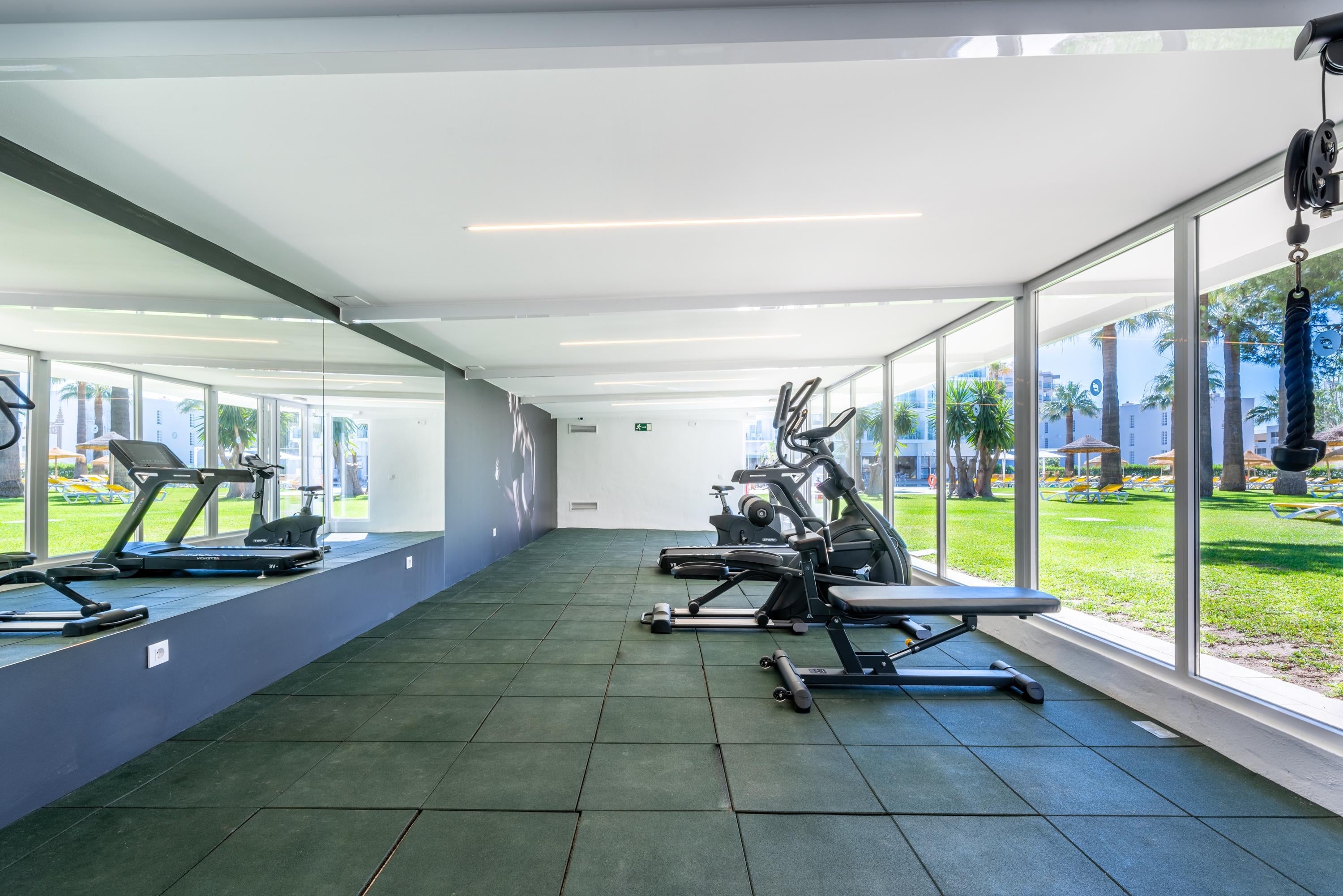 Gimnasio moderno en Dorobe: Hotel San Fermin, con vistas a la piscina y palmeras.