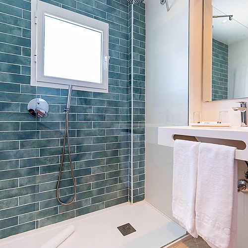 Modern bathroom Dorobe: Hotel San Fermin con ducha de azulejos verde azulado y lavabo blanco con toallas.