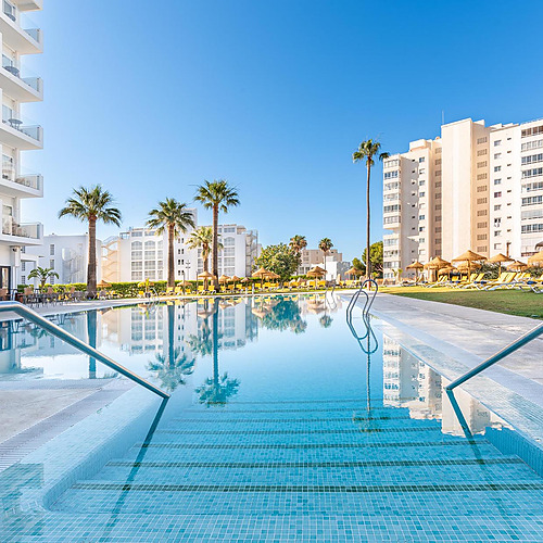 Piscina de hotel con tumbonas, palmeras y edificios Dorobe: Hotel San Fermin.