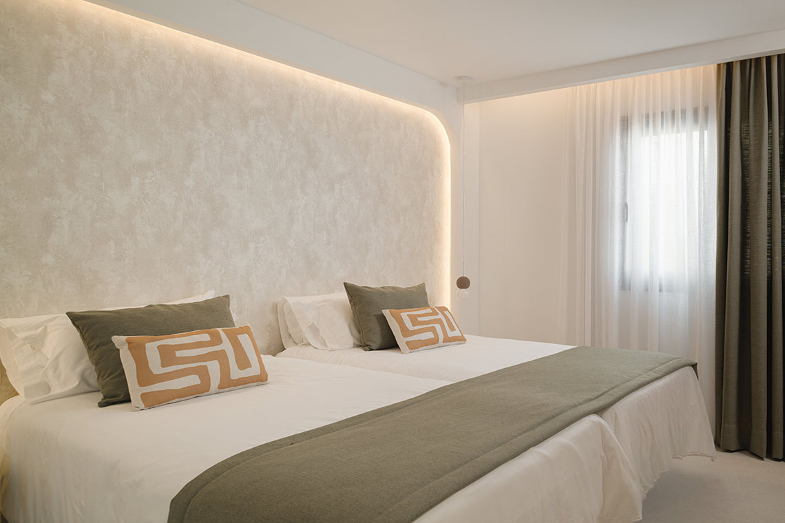 Modern bedroom with king bed, patterned wall, and TV. Sands Beach