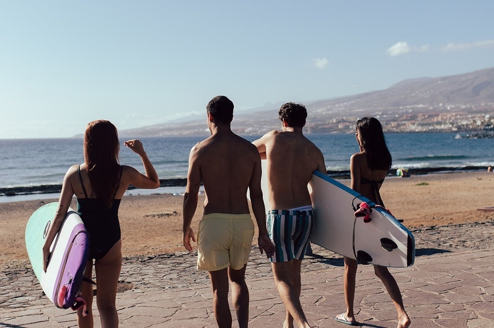 dos hombres y dos mujeres caminan por la playa con tablas de surf