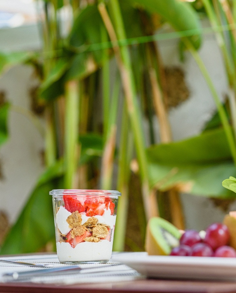 una mesa con un plato de frutas y un vaso de yogur