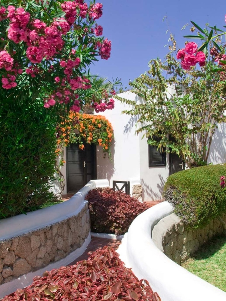 una casa blanca rodeada de flores rosas y arbustos