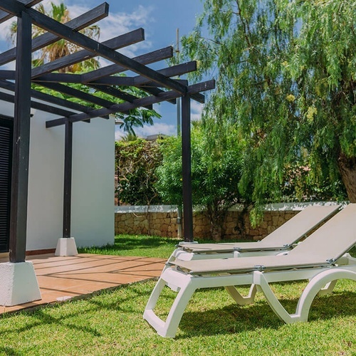 two white lounge chairs under a pergola in a garden