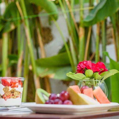 a glass of yogurt with strawberries and granola next to a plate of fruit
