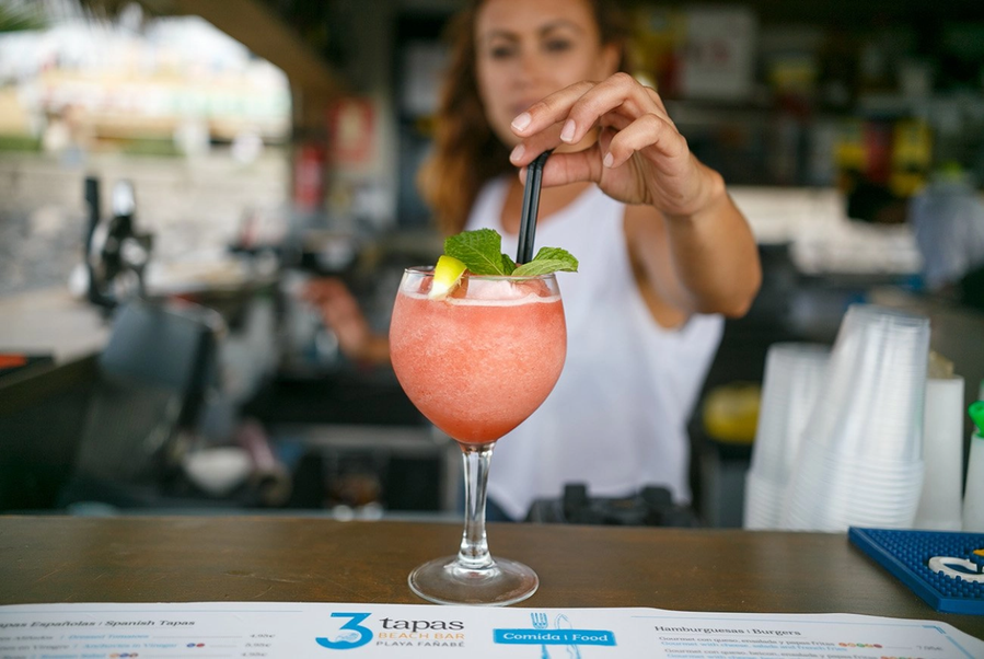 una persona sostiene un cóctel frente a una piscina infinita