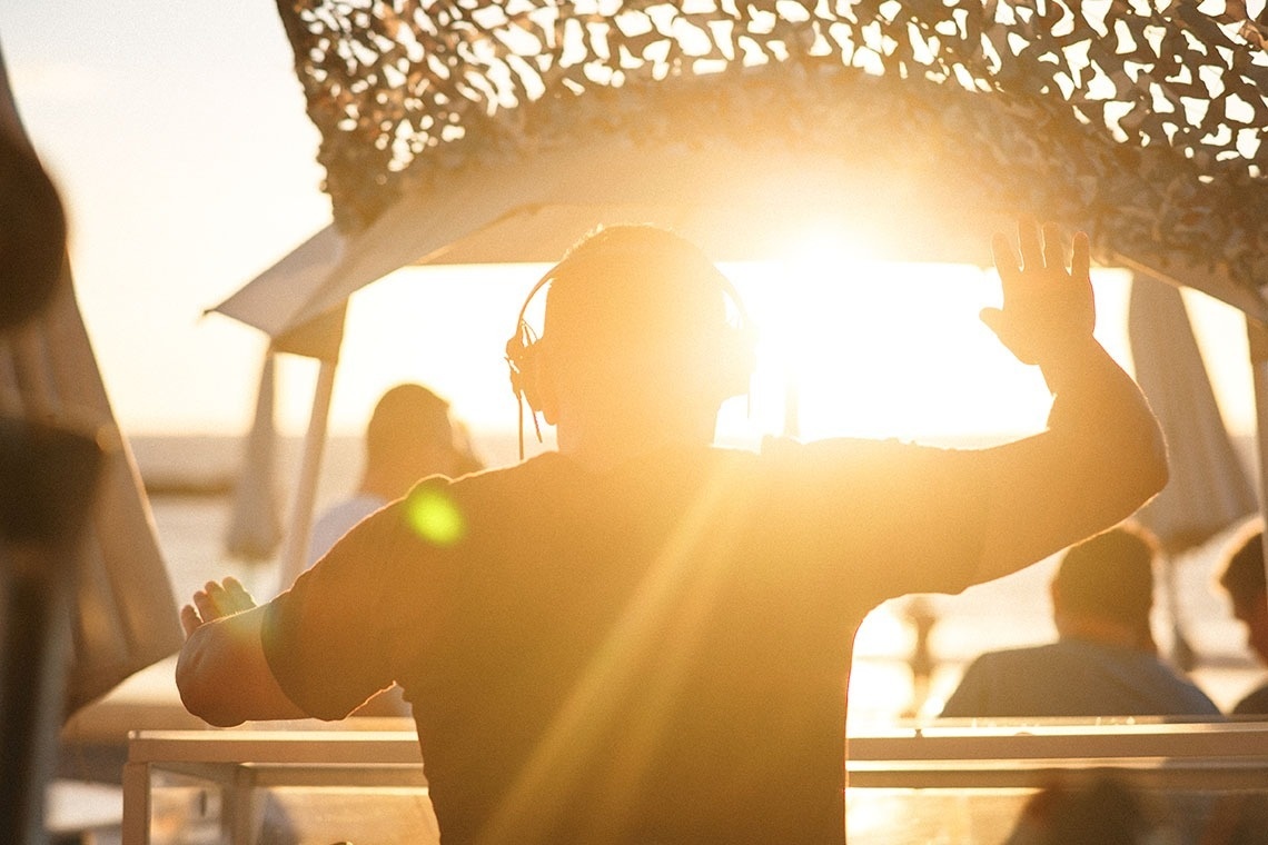 a man wearing headphones stands in front of a sunset