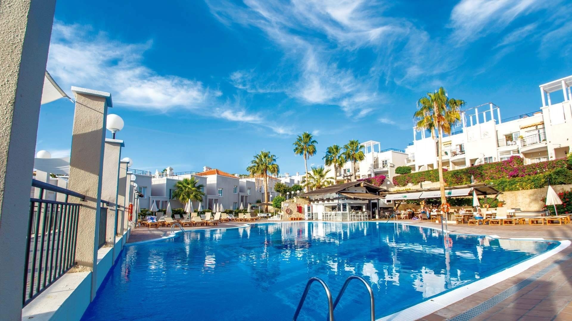 a large swimming pool surrounded by white buildings and palm trees