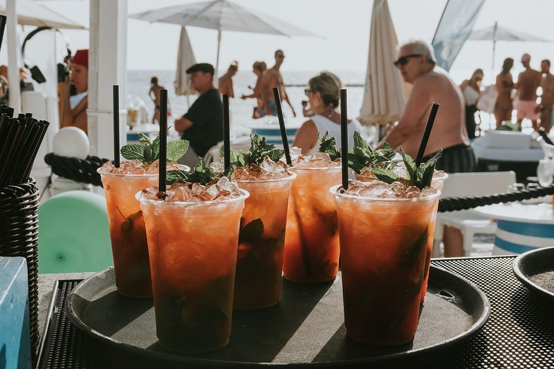 a tray of drinks with straws on the beach
