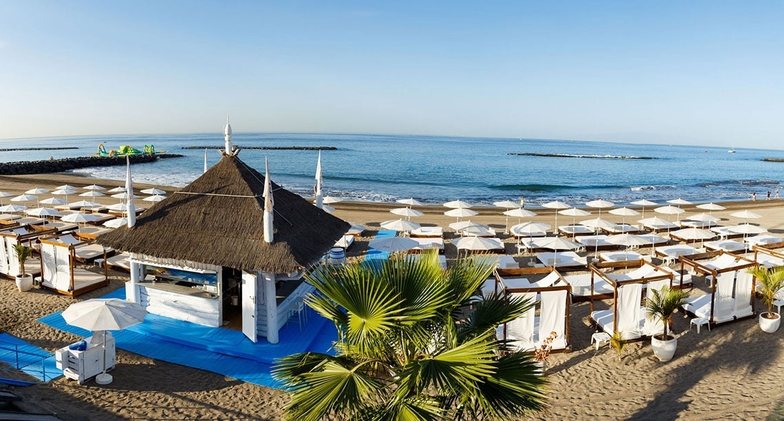 a beach with white umbrellas and a thatched hut