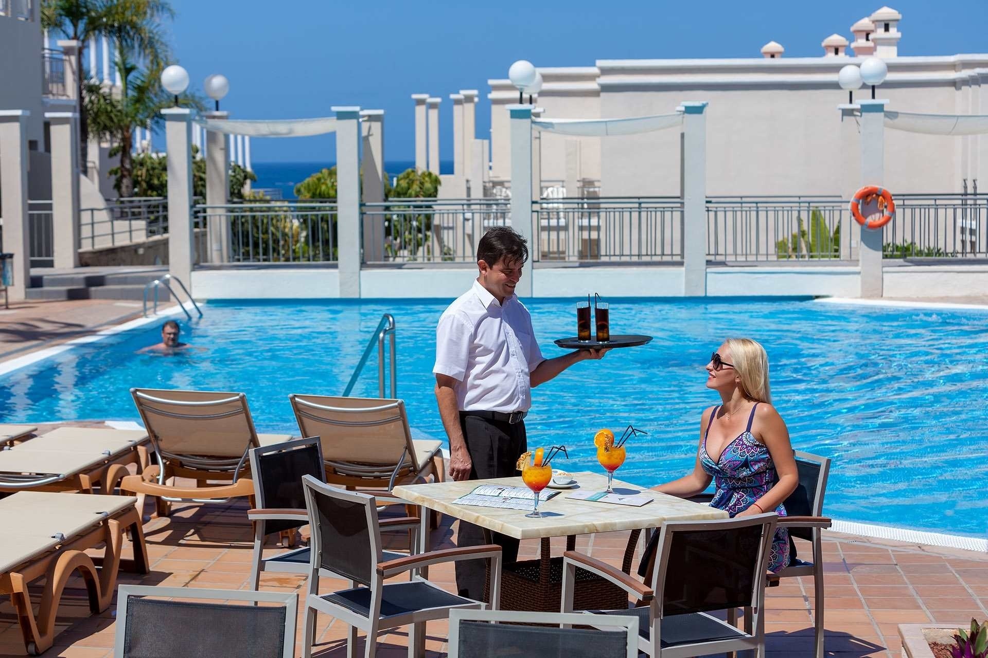 a man serving drinks to a woman by a pool