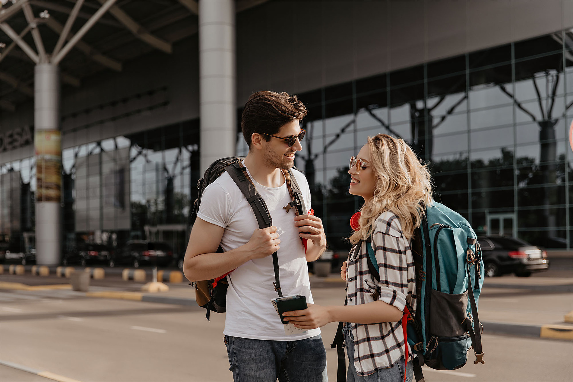 Pareja @Sand & Sea: Corporativa con mochilas en el aeropuerto, emocionados por su viaje.