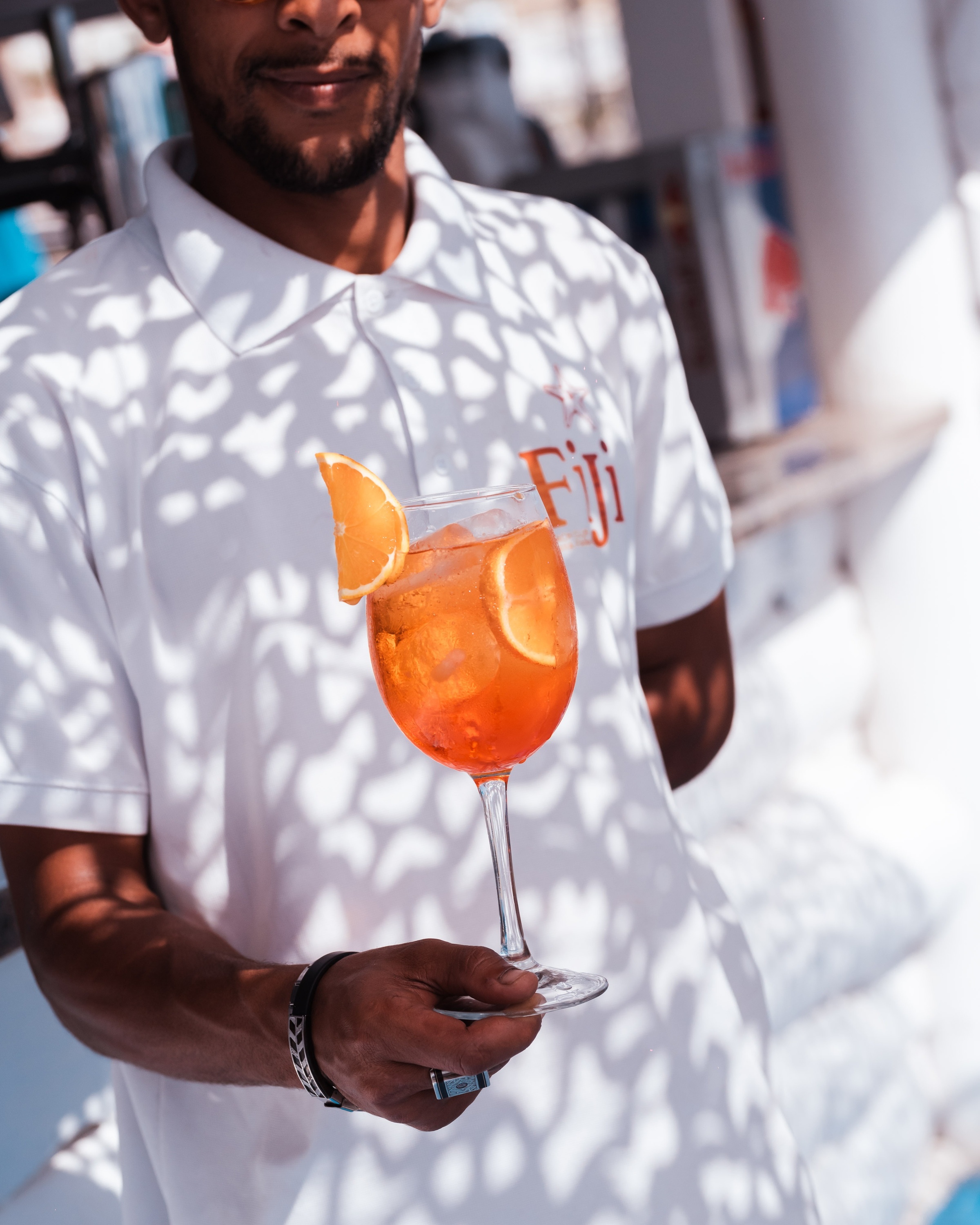 a man wearing a fiji shirt holds a glass of orange juice
