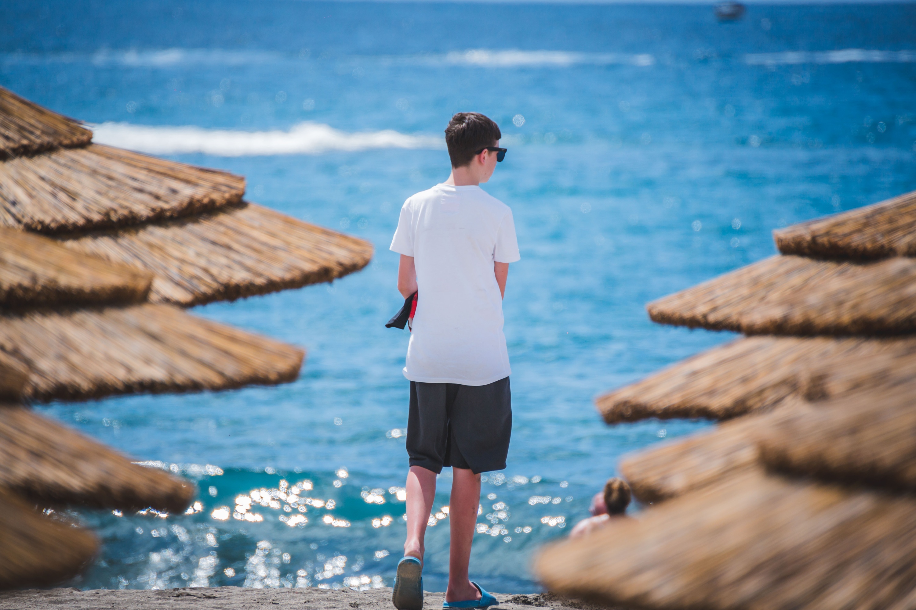 a boy in a white shirt and black shorts is walking on the beach
