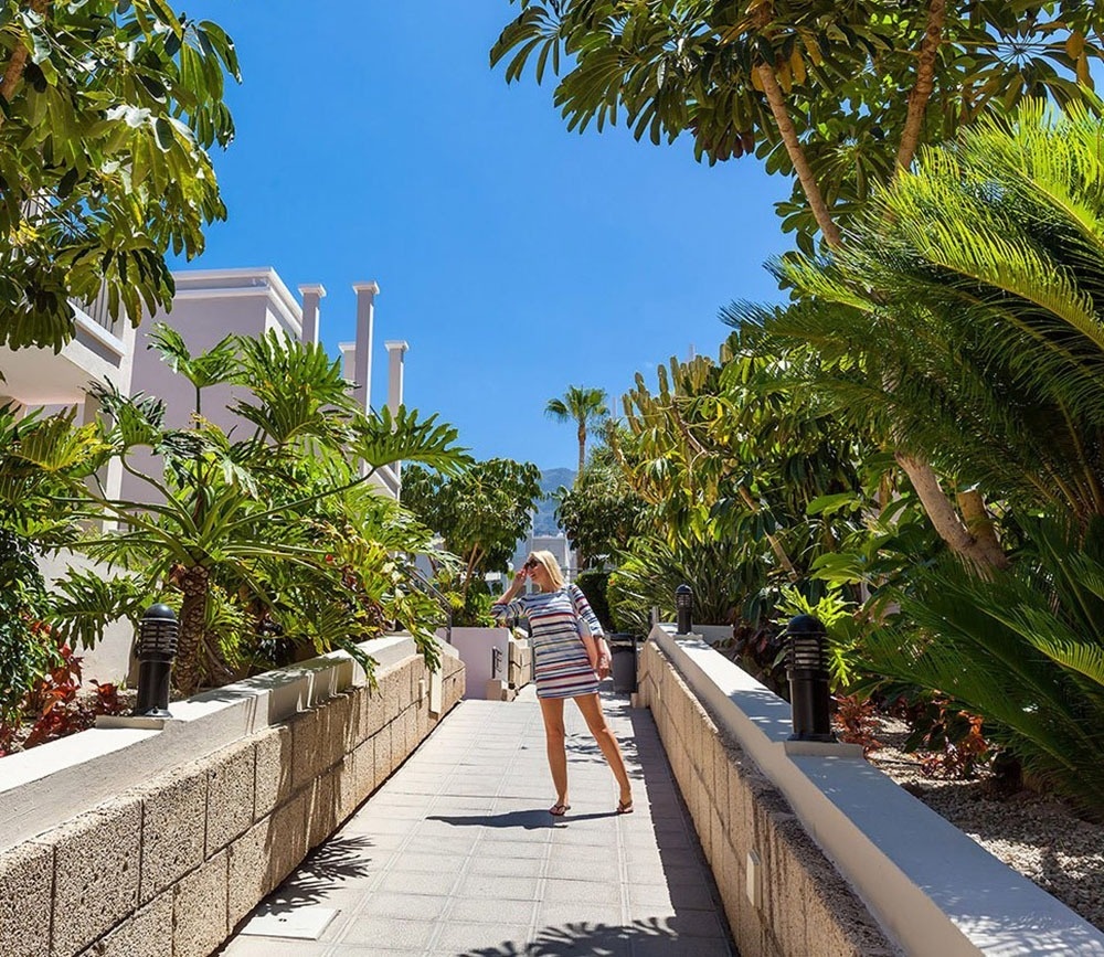 a woman in a striped dress walks down a walkway surrounded by palm trees