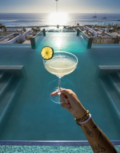 a person holding a martini in front of an infinity pool