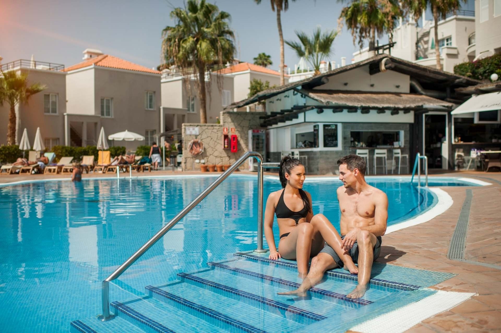 a man and a woman sit on the steps of a swimming pool