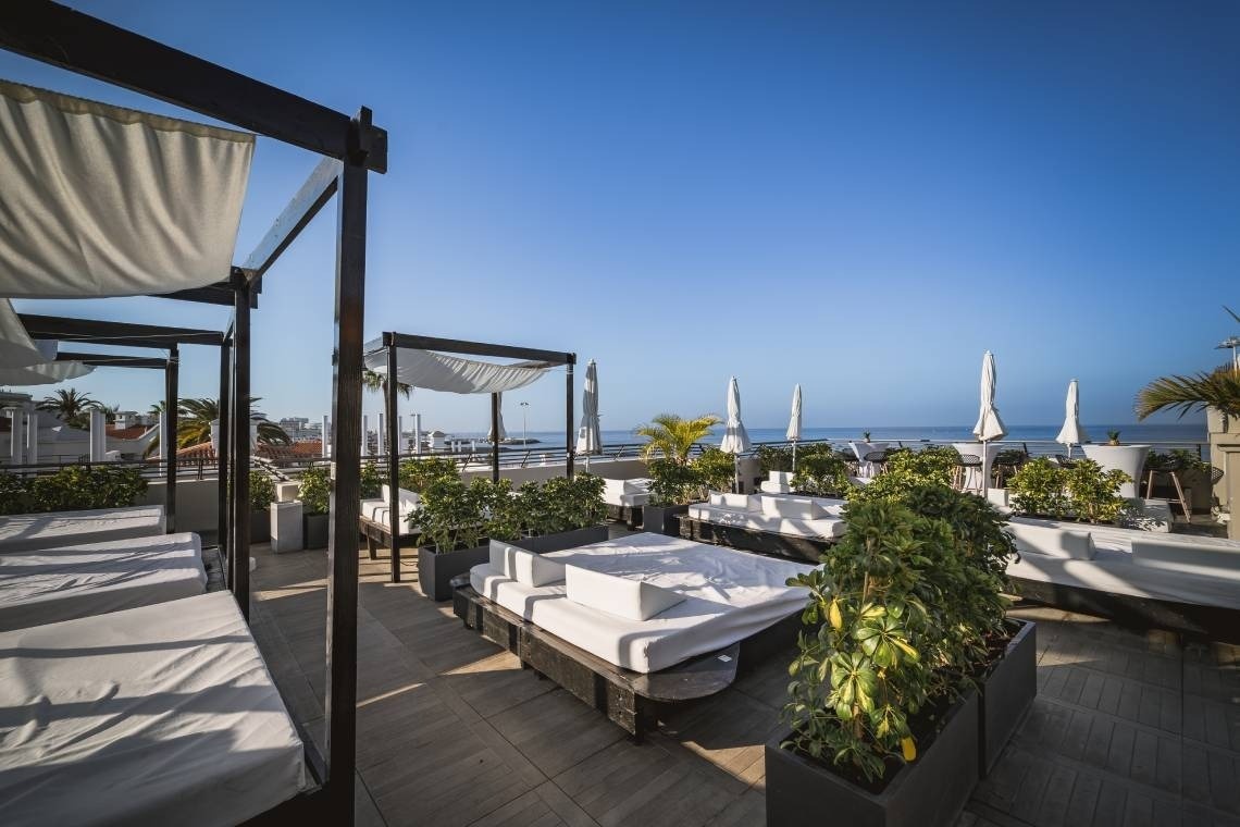 Terraza de azotea de hotel con camas balinesas y vista al mar.