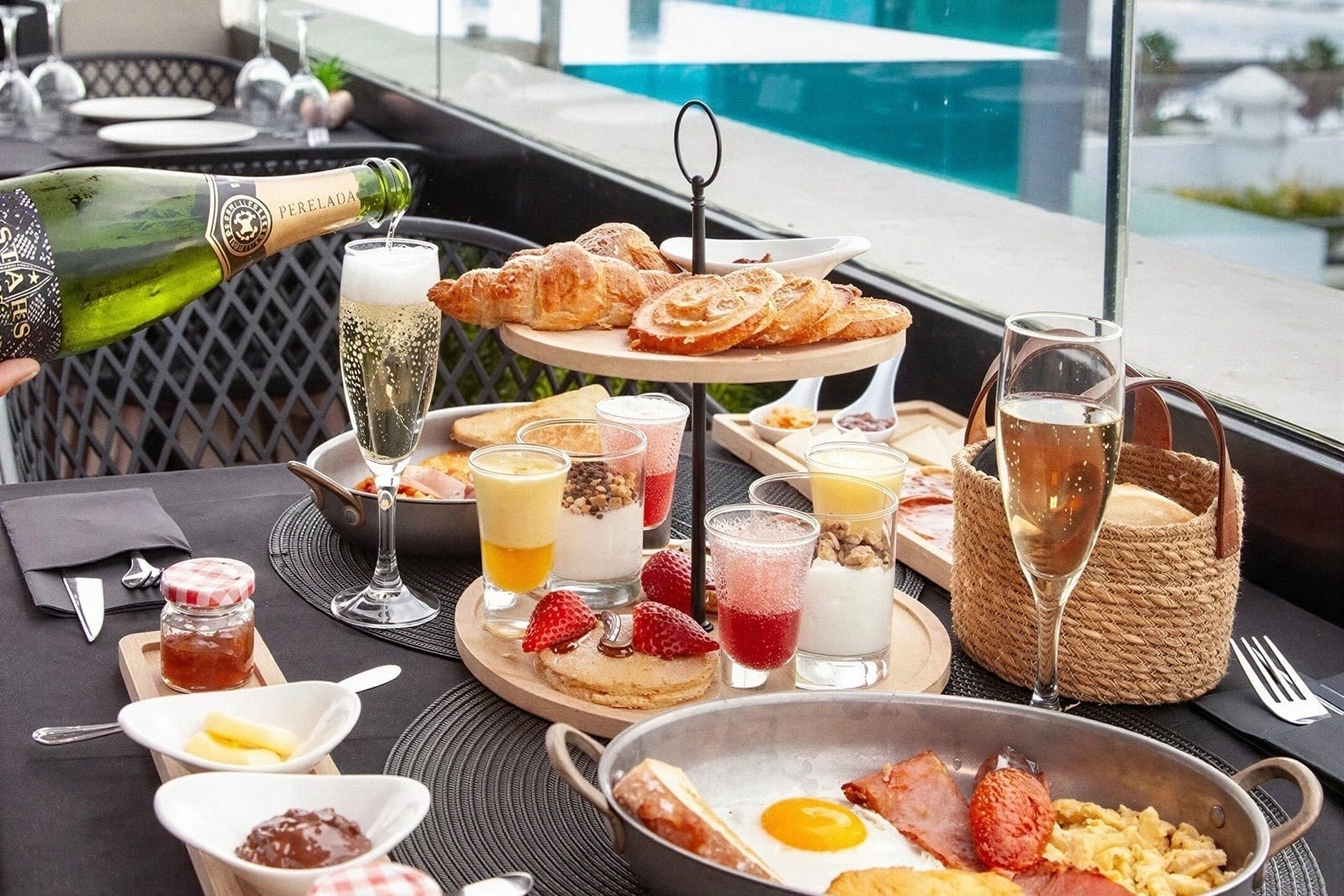 Desayuno de lujo en hotel con champán, bollería, huevos y vista a la piscina.