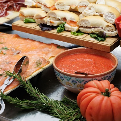 a bowl of tomato soup sits next to a tray of salmon