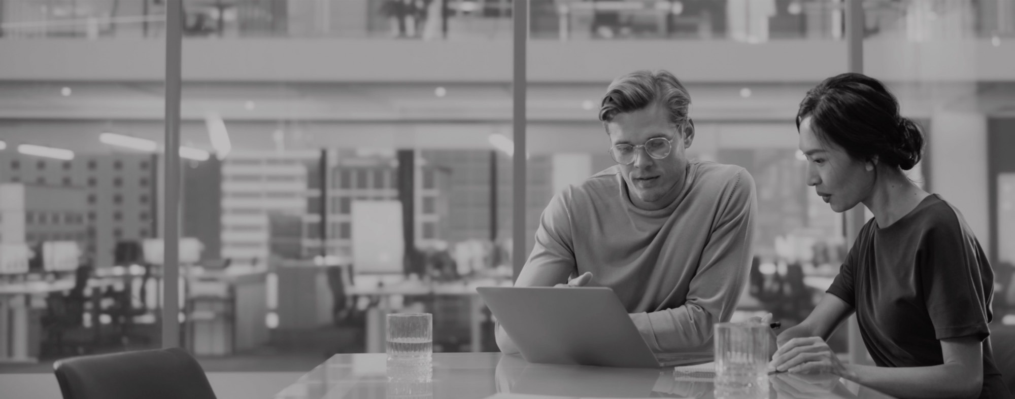 a man and a woman sit at a table looking at a laptop