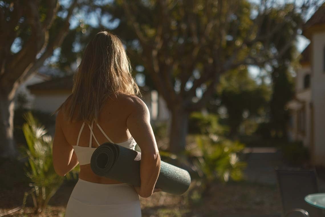 una mujer lleva una estera de yoga sobre sus hombros
