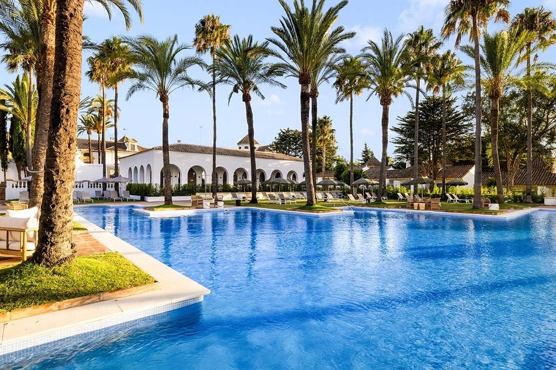 una gran piscina rodeada de palmeras y un edificio blanco