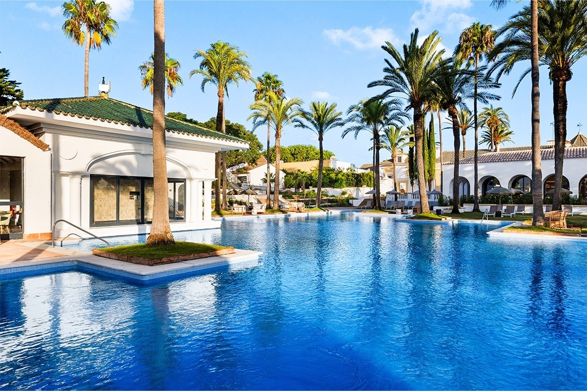 a large swimming pool surrounded by palm trees and umbrellas