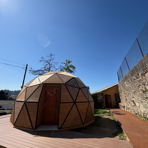 Quinta São Miguel de Arcos: cúpula geodésica de madeira com porta, deck de madeira e céu azul.