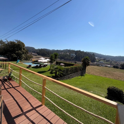Vista de um deck de madeira para uma área de piscina com espreguiçadeiras, gramado e paisagem rural. Quinta São Miguel de Arcos