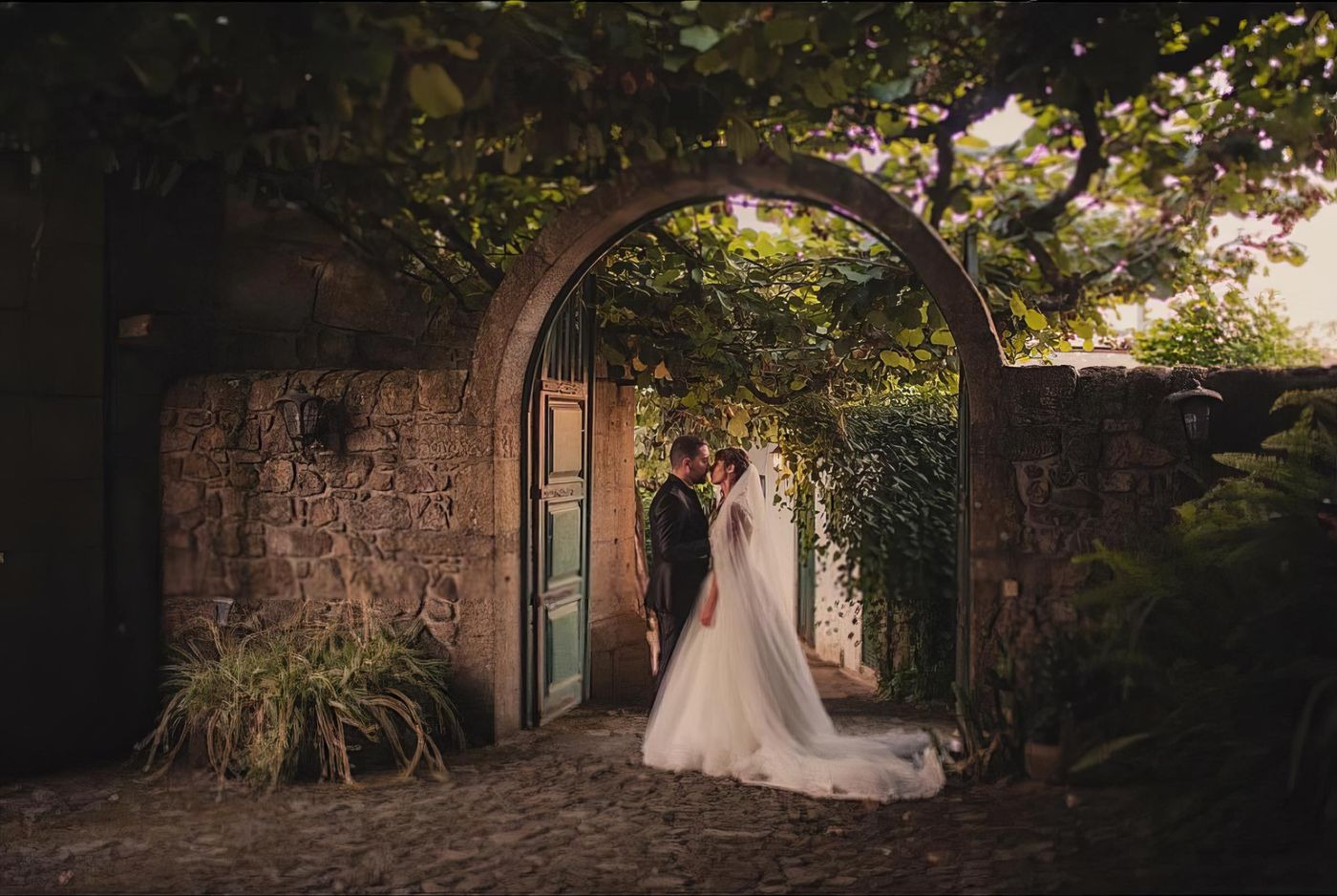Casal sob arco em pedra com vegetação trepadeira.