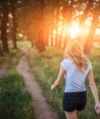 uma mulher está andando por um caminho na floresta ao pôr do sol .