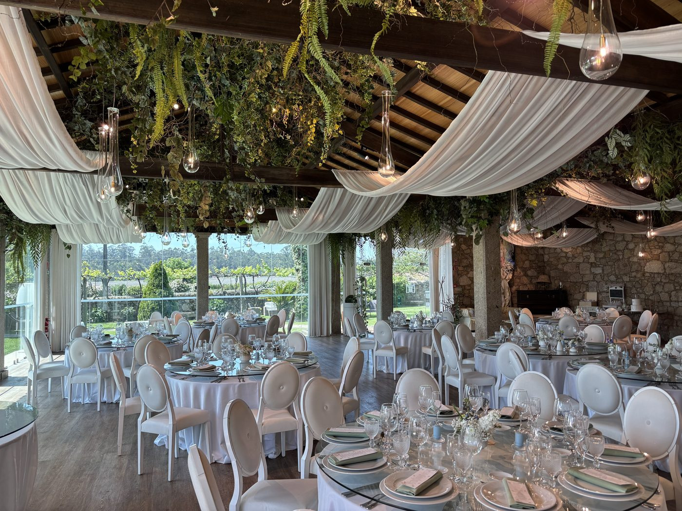 Salão rústico em pedra da Quinta São Miguel de Arcos, decorado para casamento, com mesas postas, drapeados e vegetação suspensa.
