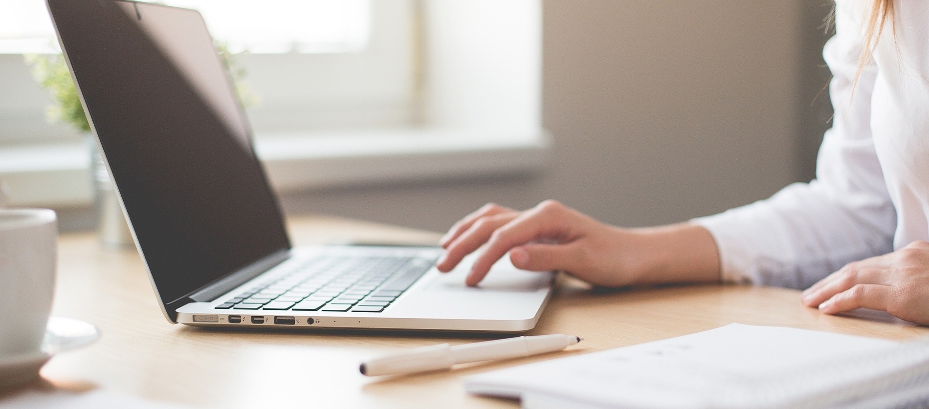 a person is typing on a laptop with a pen next to it