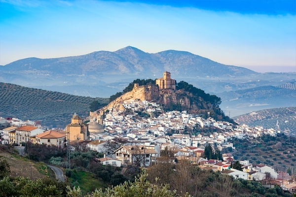 a small town sits on top of a hill with mountains in the background