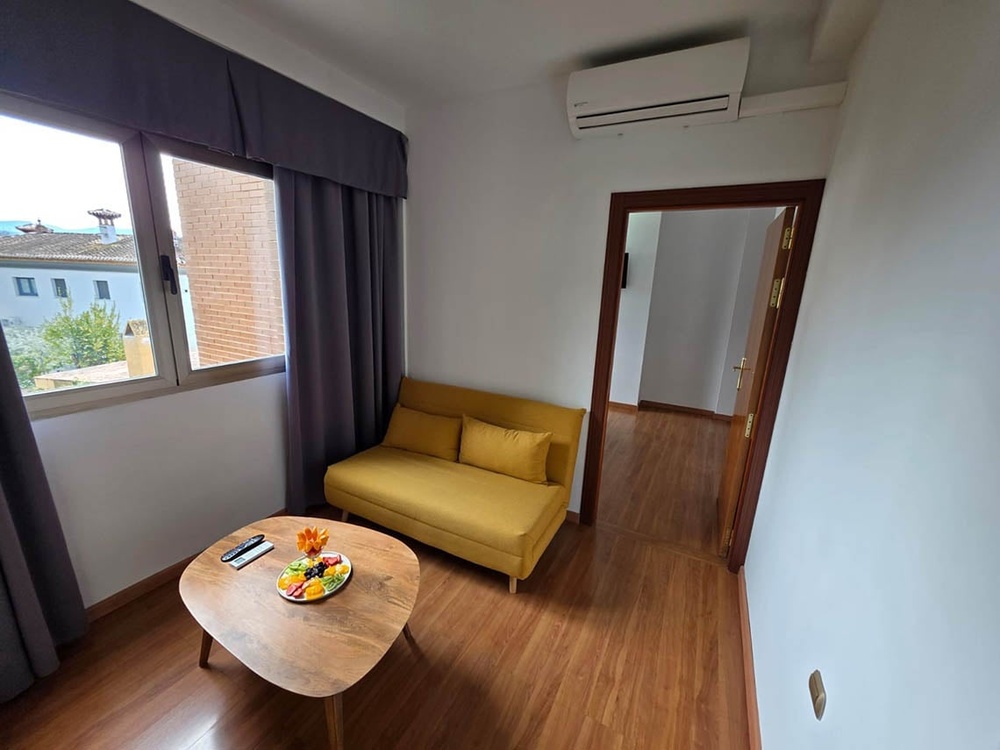 Modern Hotel Saylu room with cozy yellow sofa, fruit platter, and scenic window view.