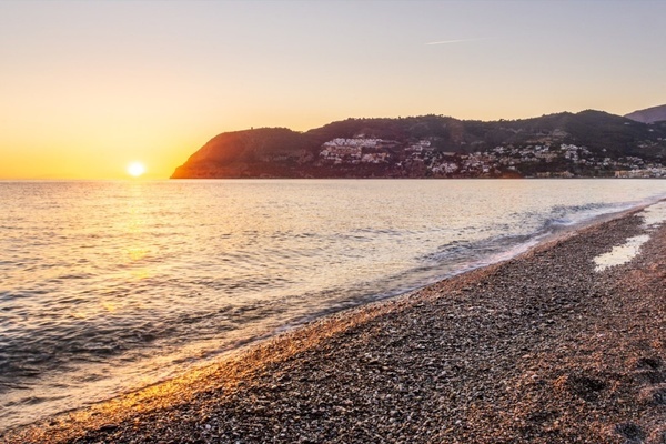 a sunset over a body of water with mountains in the background