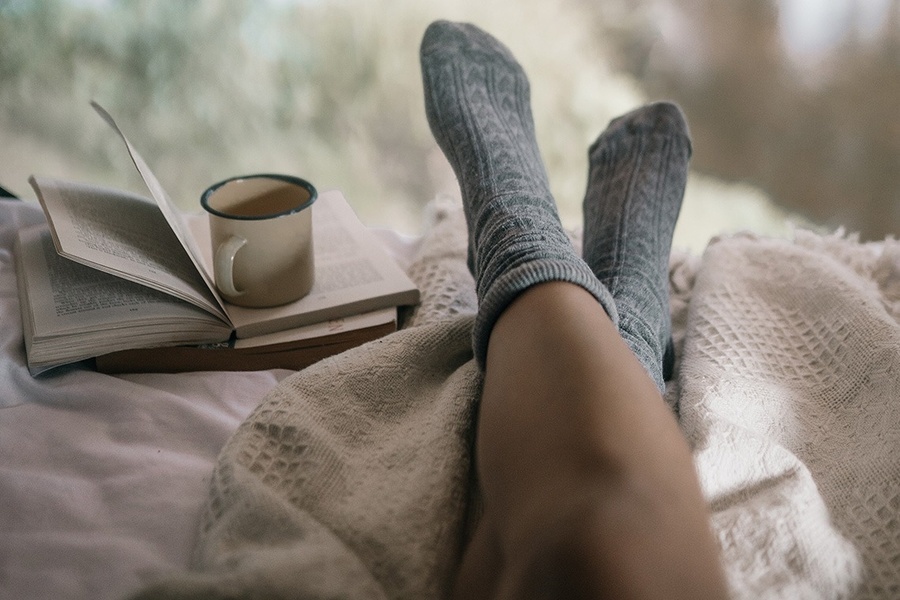 a person laying on a bed with a book and a cup of coffee